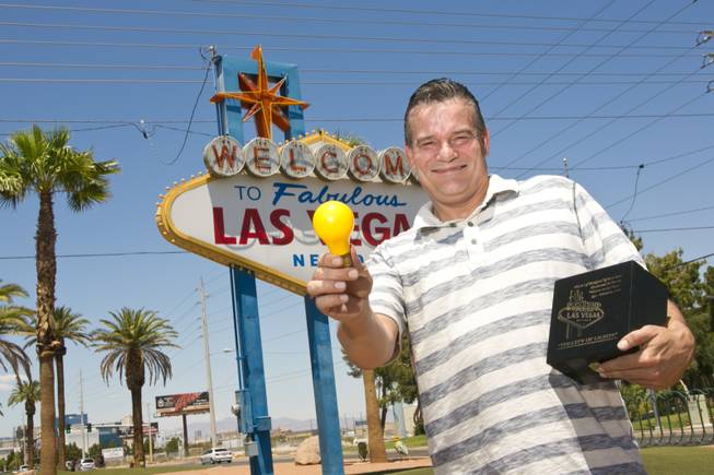 Russell Millar shows off a souvenir lightbulb that he sells, which came right off the famous "Welcome To Las Vegas" sign behind him, Monday July 9, 2012.